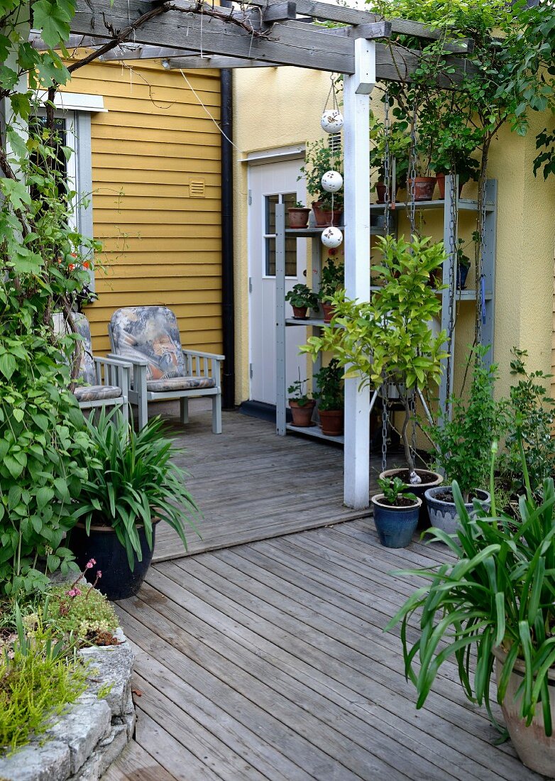 Blick vom Garten auf Veranda mit Holzboden, an gelber Holzfassade Armlehnstühle