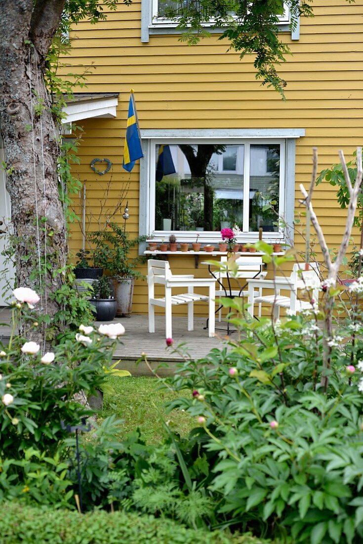 weiße Gartenmöbel auf Terrasse vor gelb gestrichener Holzhaus