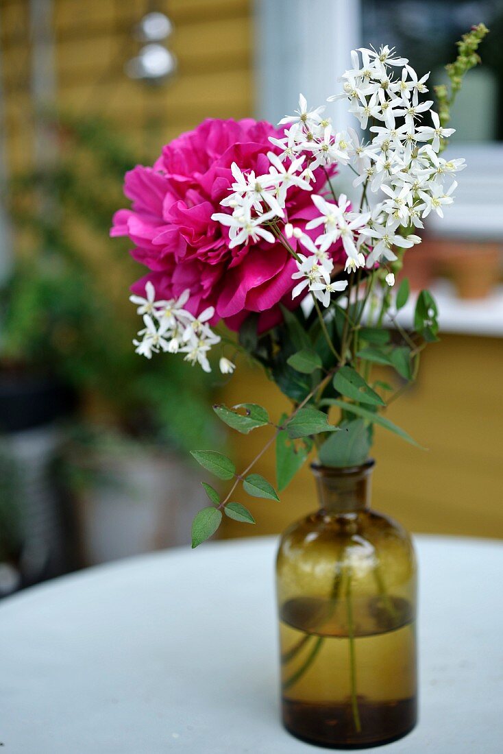 Sommerblumen in Apothekerflasche auf Gartentisch
