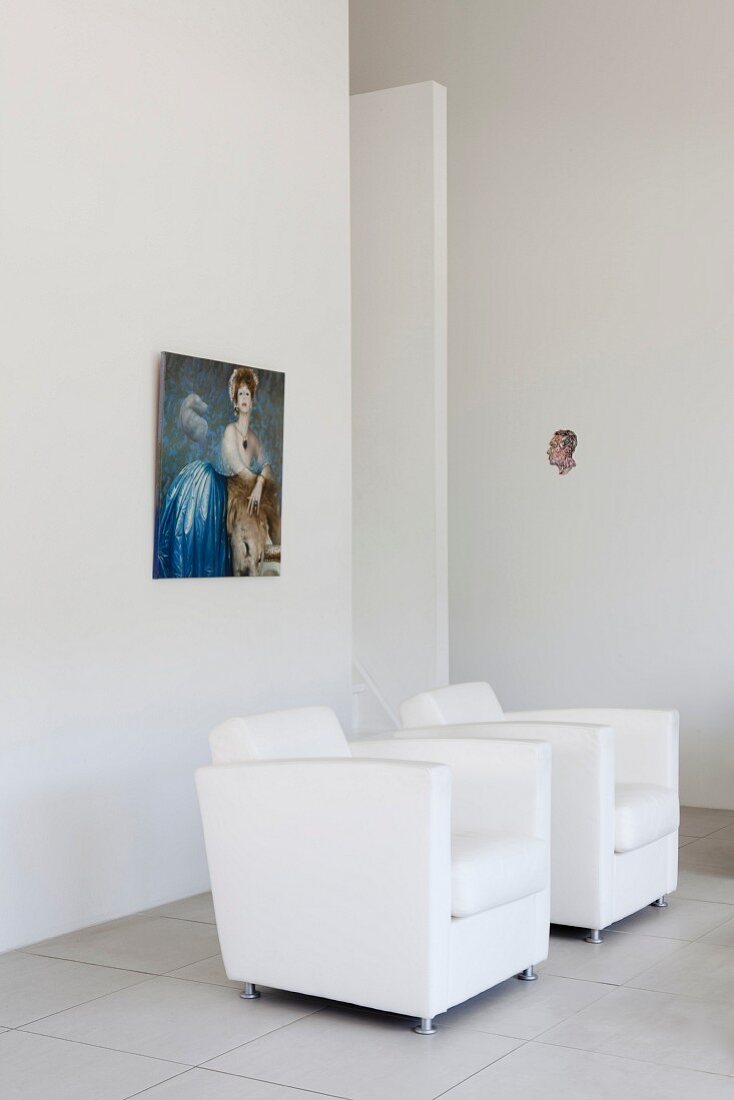 White, designer armchairs below picture on wall in minimalist interior