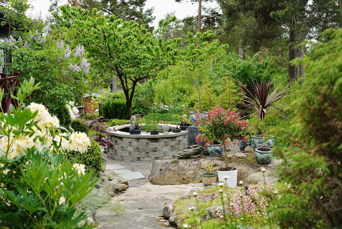 Pond in stone surround and Chinese pots on gravel area in landscaped garden