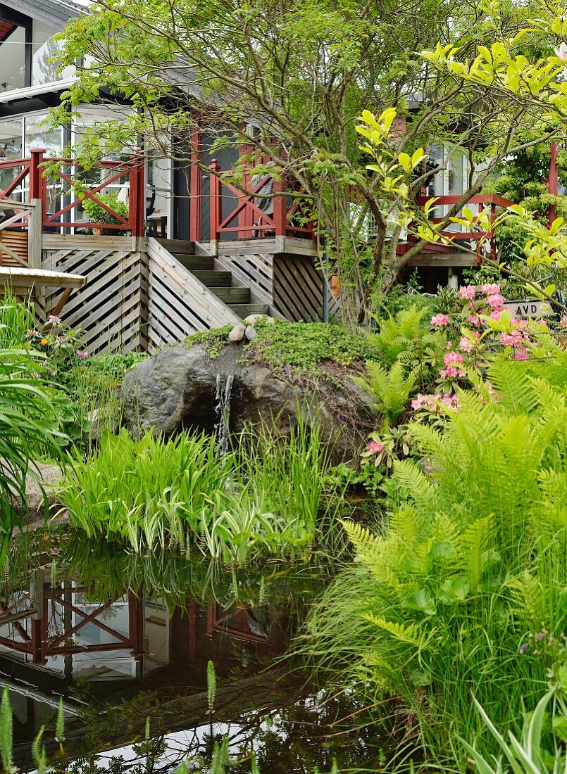 Pond with waterfall emerging from boulder in front of Scandinavian wooden house