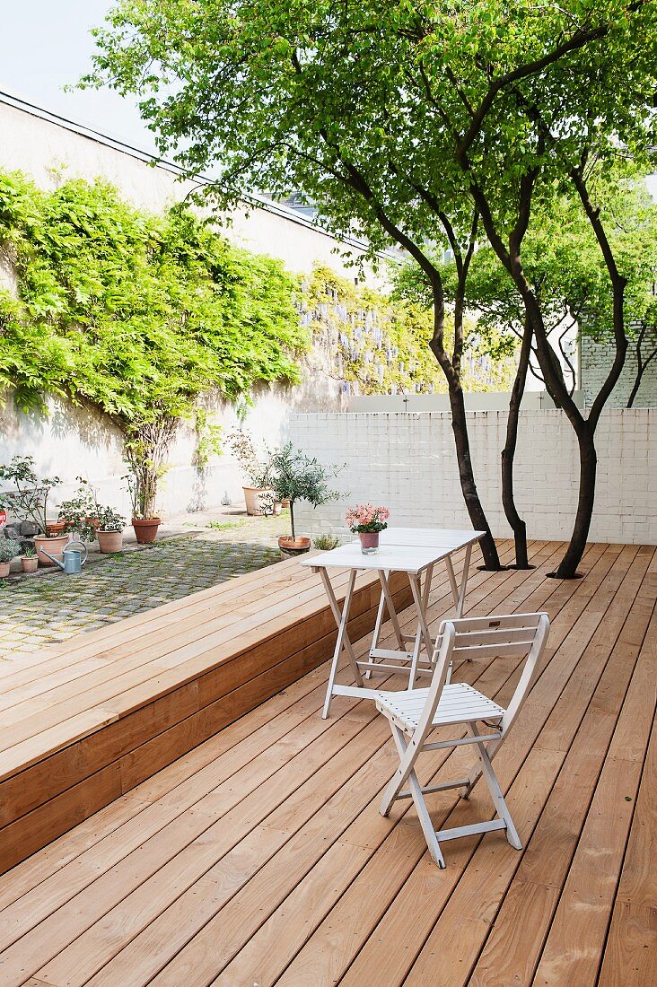 Schlichter Gartenstuhl und Tisch auf Holzterrasse, mit integrierter Bank, im Innenhof mit begrünter Wand