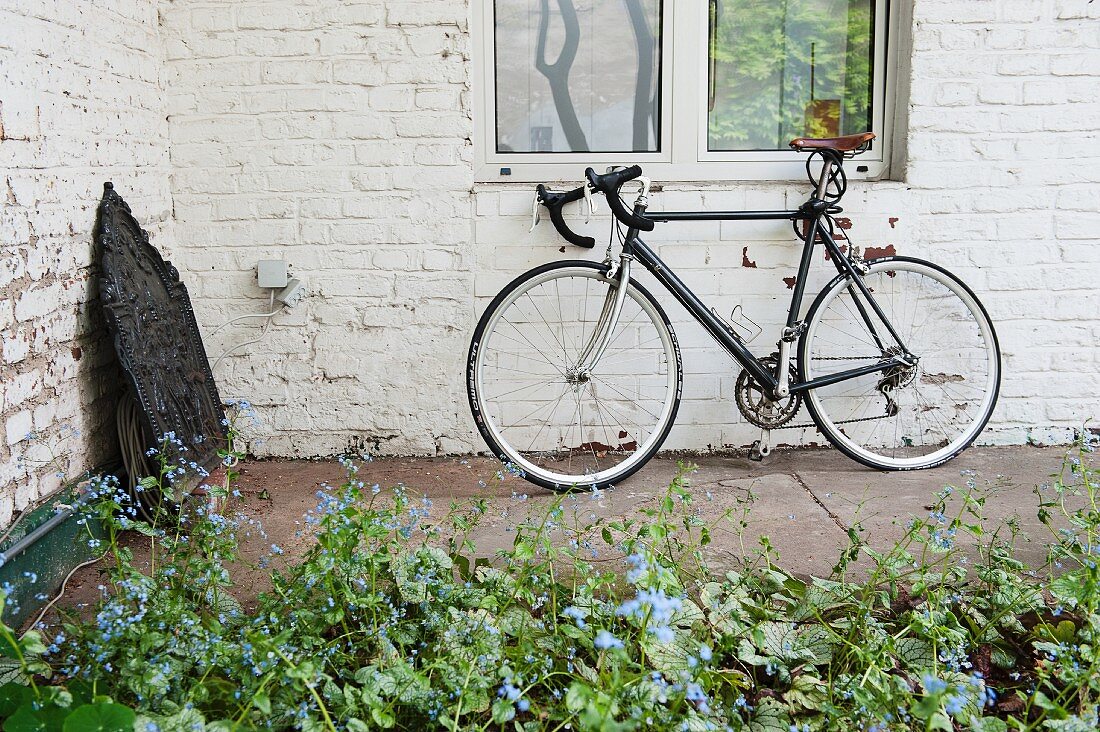 An geweisselter Ziegelwand lehnendes Fahrrad, davor Blumenbeet