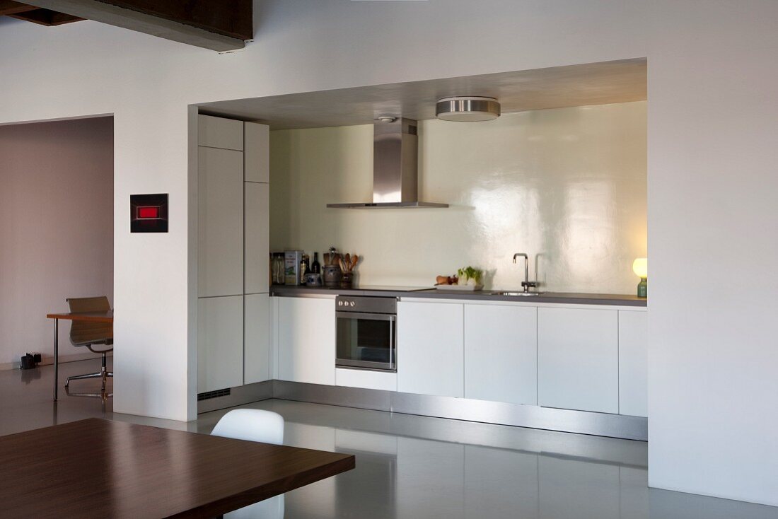 View from dining area into open-plan, white kitchen with illuminated niche