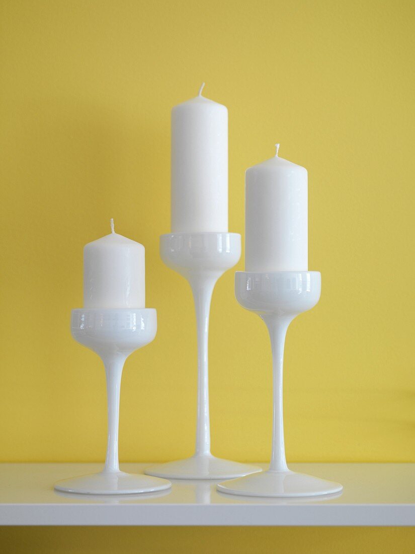 White candles in three-piece, white china candlestick set against yellow wall