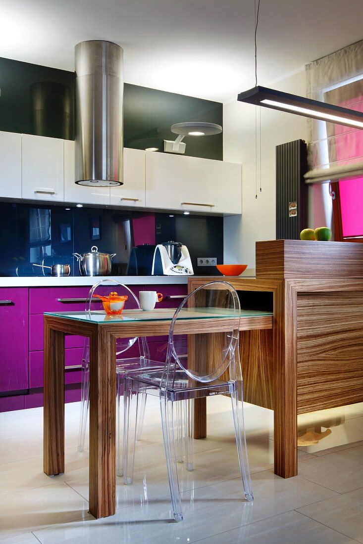 Wooden counter with extendable table and ghost chair; fitted kitchen with bold accents of colour in background