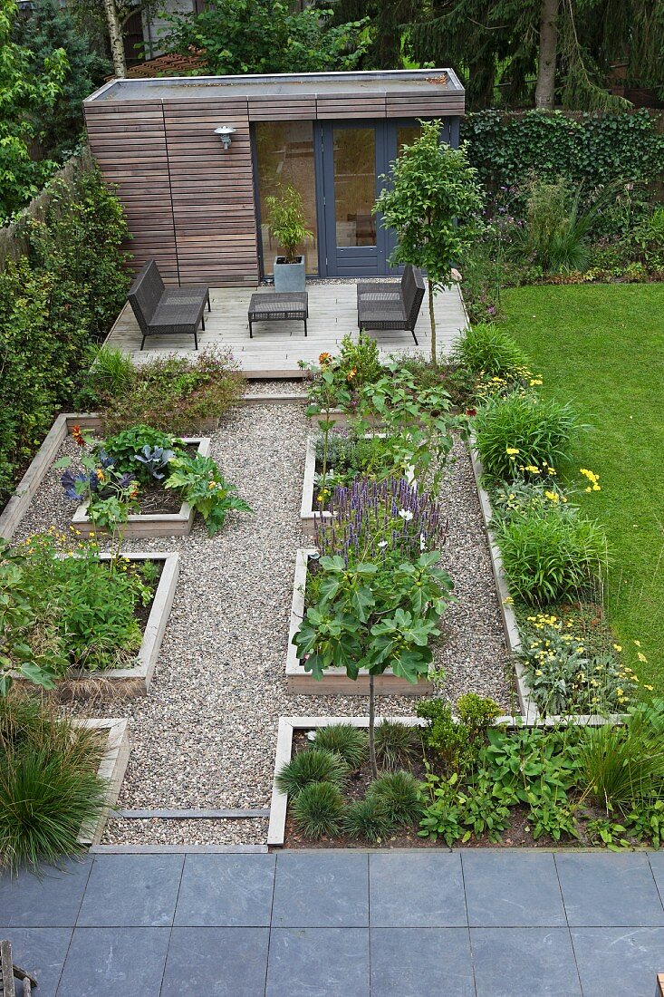 Geometrisch angelegte Hochbeete auf gekiestem Platz, im Hintergrund Terrasse mit modernen Outdoor-Möbeln und Gartenhäuschen