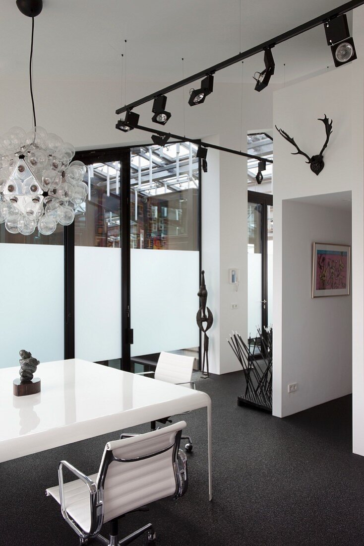 Weisser Tisch mit eleganten Bürostühlen und schwarzes Licht-Schienensystem mit Strahlern in Loftwohnung