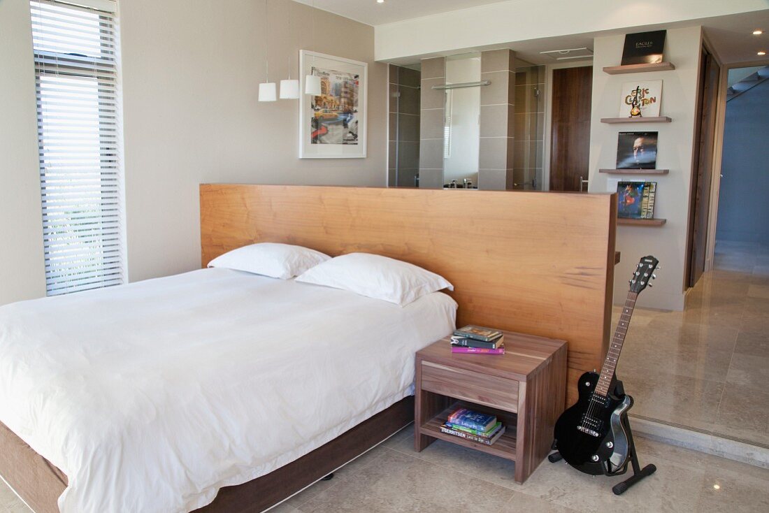 Electric guitar next to bedside table, double bed against half-height partition with desk in front of ensuite bathroom