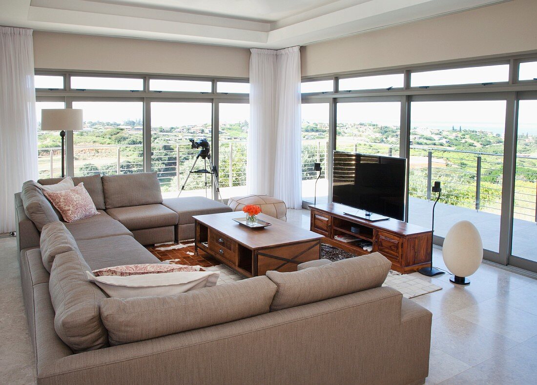 U-shaped, taupe sofa set around coffee table and flatscreen TV against continuous glass wall