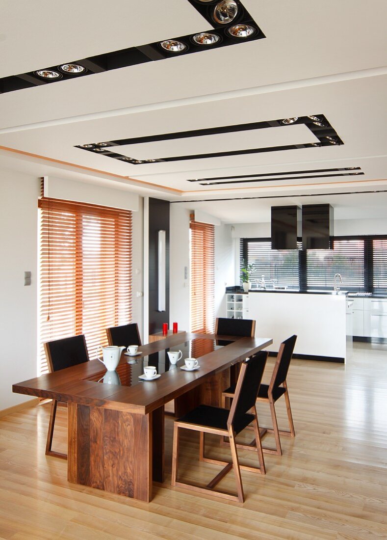 Eleganter Essplatz, lange Tafel aus Holz und Stühle im Retro Look, dahinter Kochbereich, in offenem Wohnraum mit Einbaustrahlern in Deckenfeldern