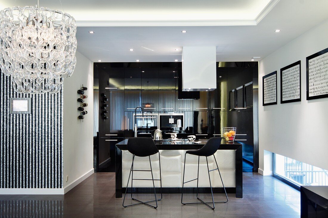 Schwarze Barhocker vor Theke in offener Küche, in modernem Wohnraum mit indirekter Deckenbeleuchtung, seitlich Kronleuchter