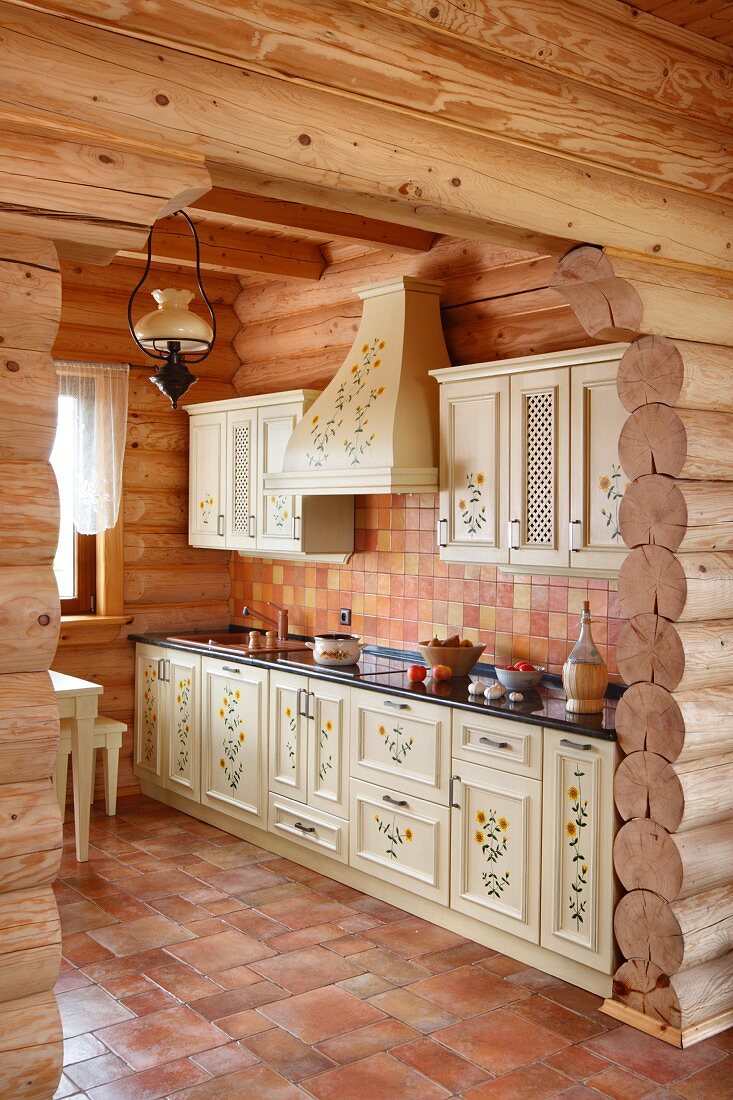 View through open doorway into rustic kitchen with terracotta floor in log cabin