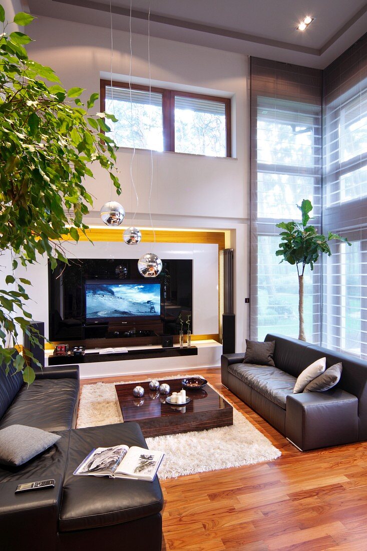 Black leather sofa set and low coffee table on flokati rug, TV in niche and transom window in high-ceilinged, elegant interior