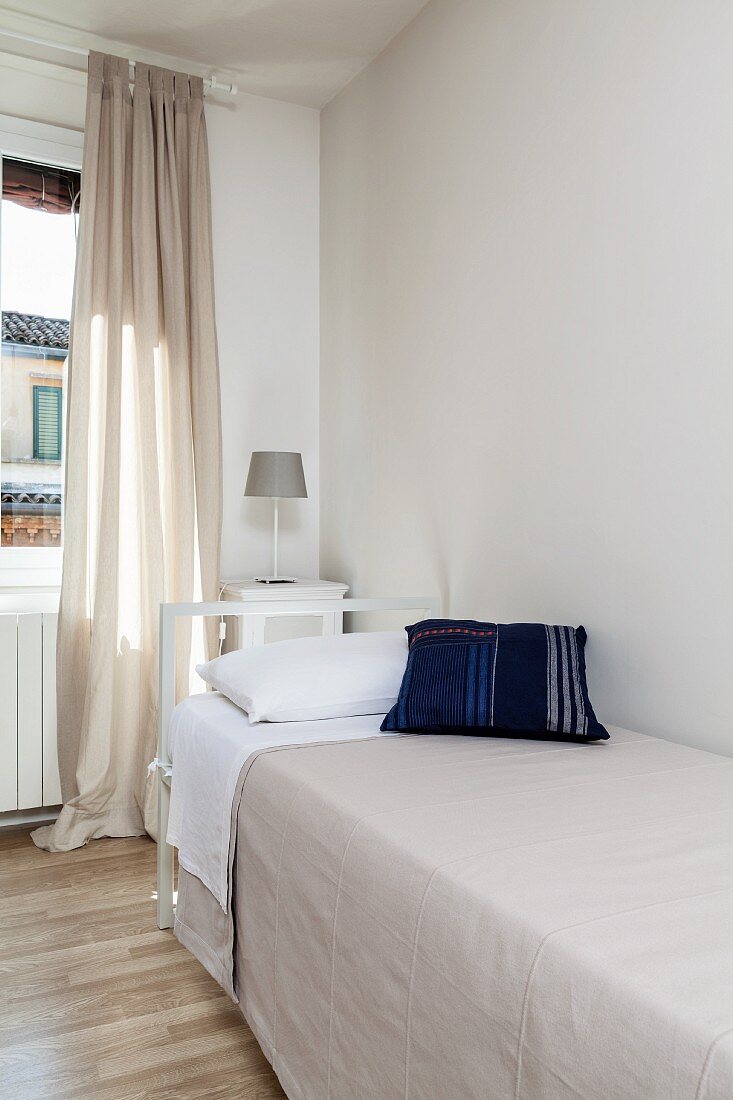 weiße Zimmerecke mit Einzelbett und bodenlangem beigefarbenem Vorhang