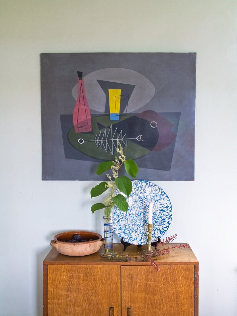 Blätterzweig in Vase und Kerzenhalter auf halbhohem Schrank aus Holz, an Wand aufgehängtes Bild