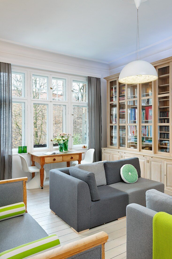 Elegantes Bibliothekzimmer mit grauen Polstersofas, Schubladentisch mit weißen Panton Stühlen in gemütlichem Altbauambiente