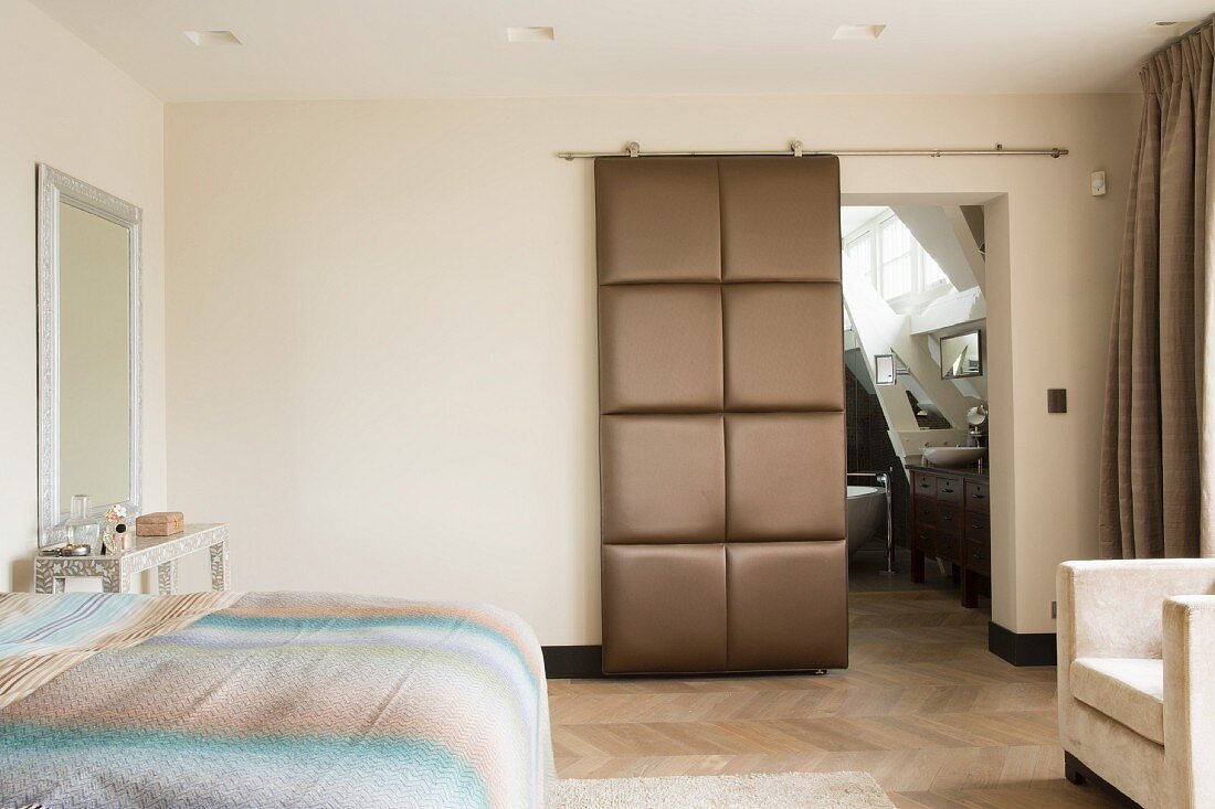 Double bed and open, upholstered sliding door leading to ensuite bathroom in bedroom