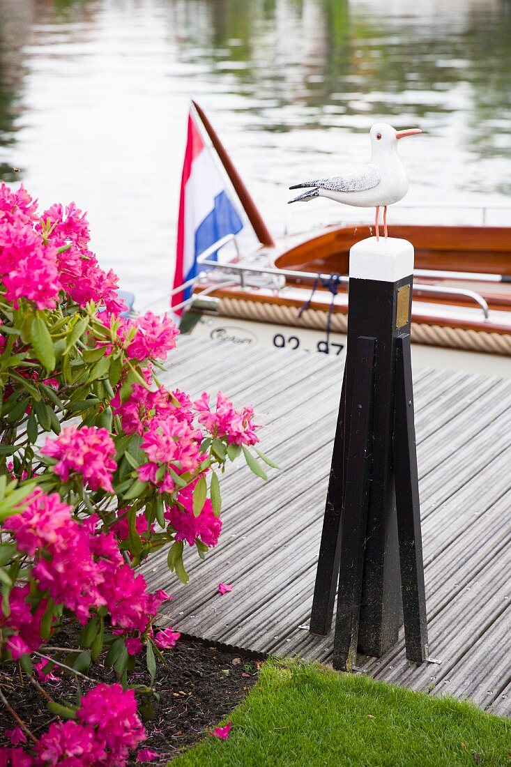 Möwenfigur auf Pfosten aus Metall auf Holzsteg, im Hintergrund teilweise sichtbares Boot