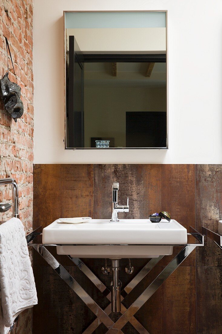 Washstand with chrome frame against rusty, Corten steel wall and below mirror in corner of bathroom