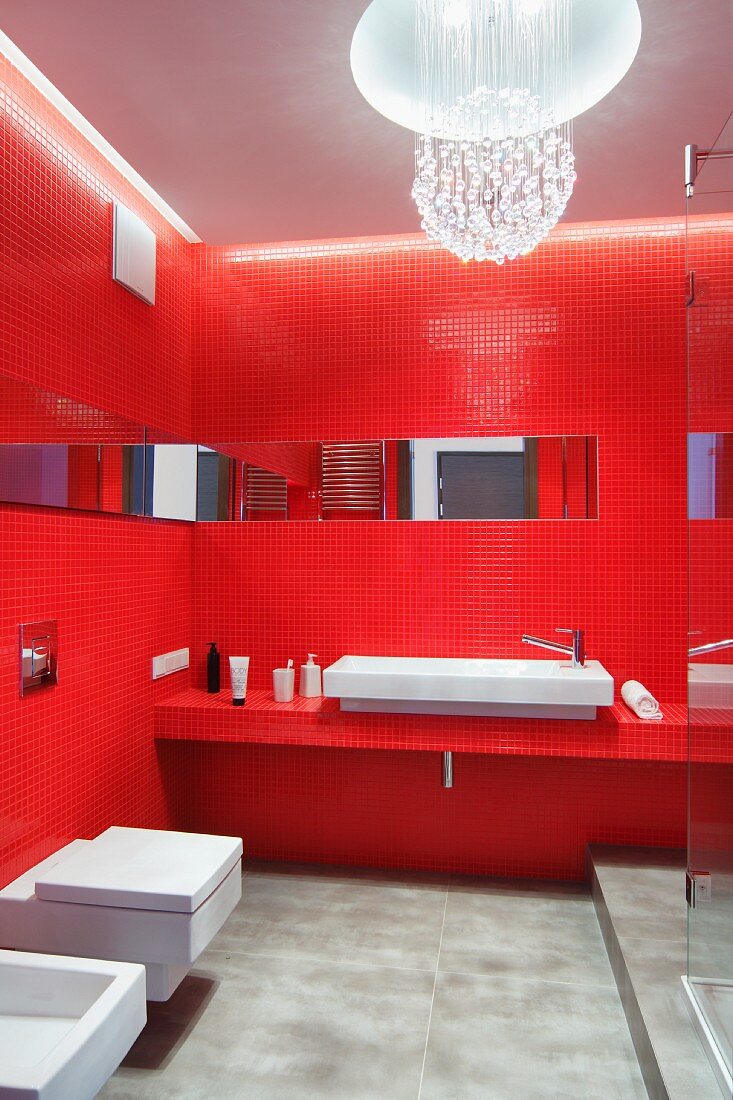 Bad in Rot - Wände und Waschtischablage mit roten Mosaikfliesen, an Decke kugelförmige Pendelleuchte aus aufgehängten Glassteinen