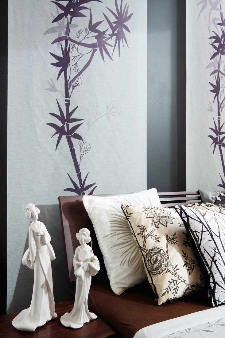 Wandbehänge mit japanischen Bambus-Zeichnungen hinter einem Doppelbett, Zierkissen und weiße Geisha-Figuren auf dem Nachttisch