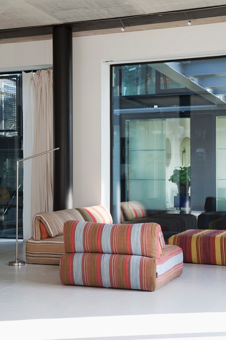 Lounge area with striped, retro floor-cushion armchairs next to glass wall in loft apartment