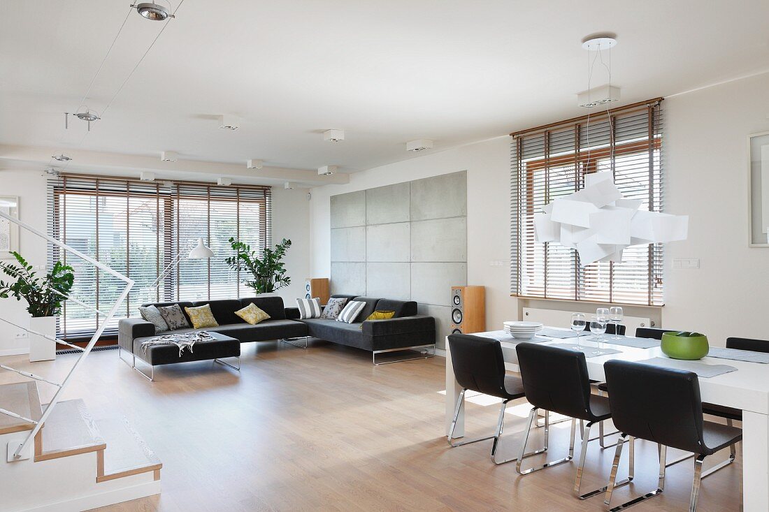 Spacious, open-plan interior; dining area with black chairs below designer light and comfortable lounge area in front of floor-to-ceiling windows