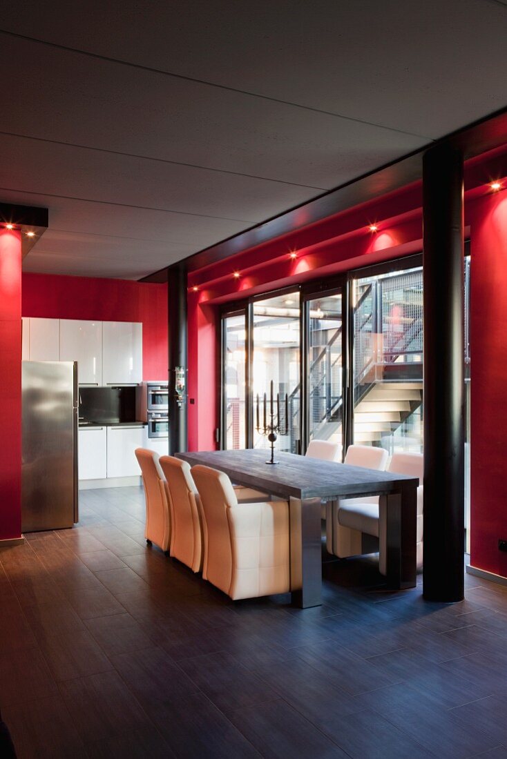 Dining area and kitchen in open-plan interior with glass wall framed in red