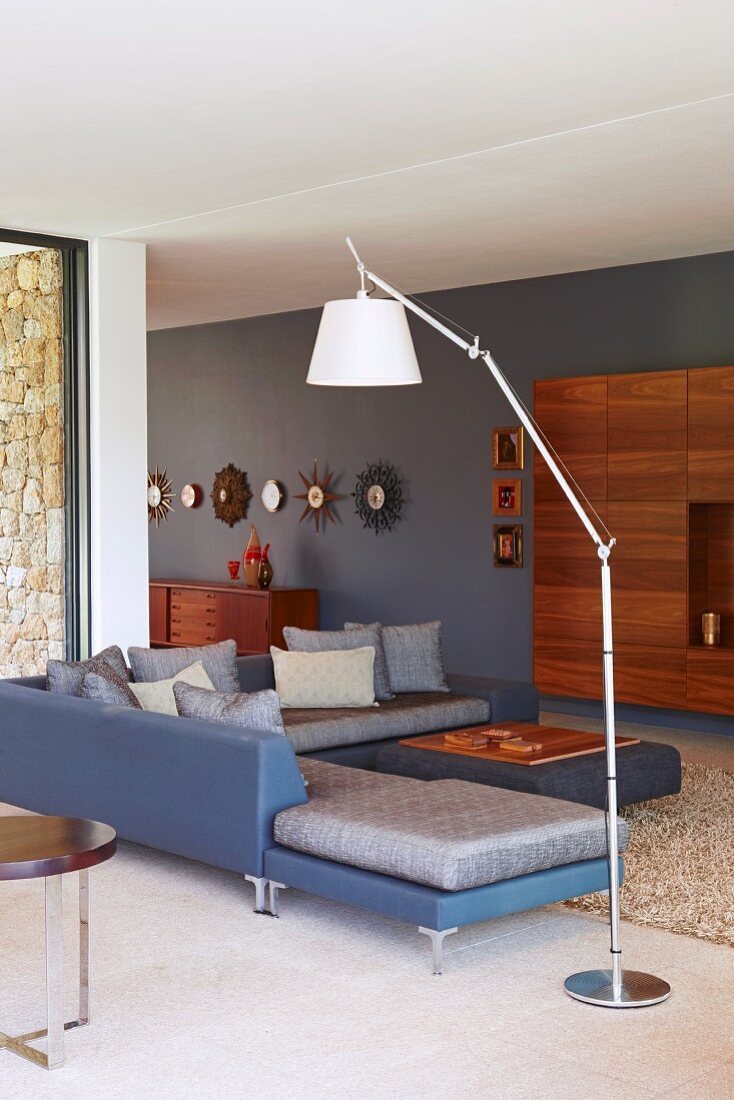 Standard lamp with white lampshade next to blue corner sofa and wall-mounted wooden cabinet in background in modern living area
