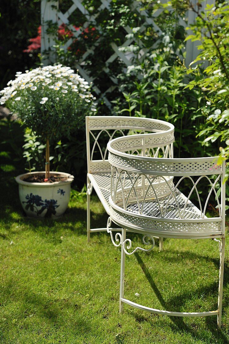 Gartenbank aus weißem, filigranem Metallgestell mit geschwungener Rückenlehne auf der Wiese