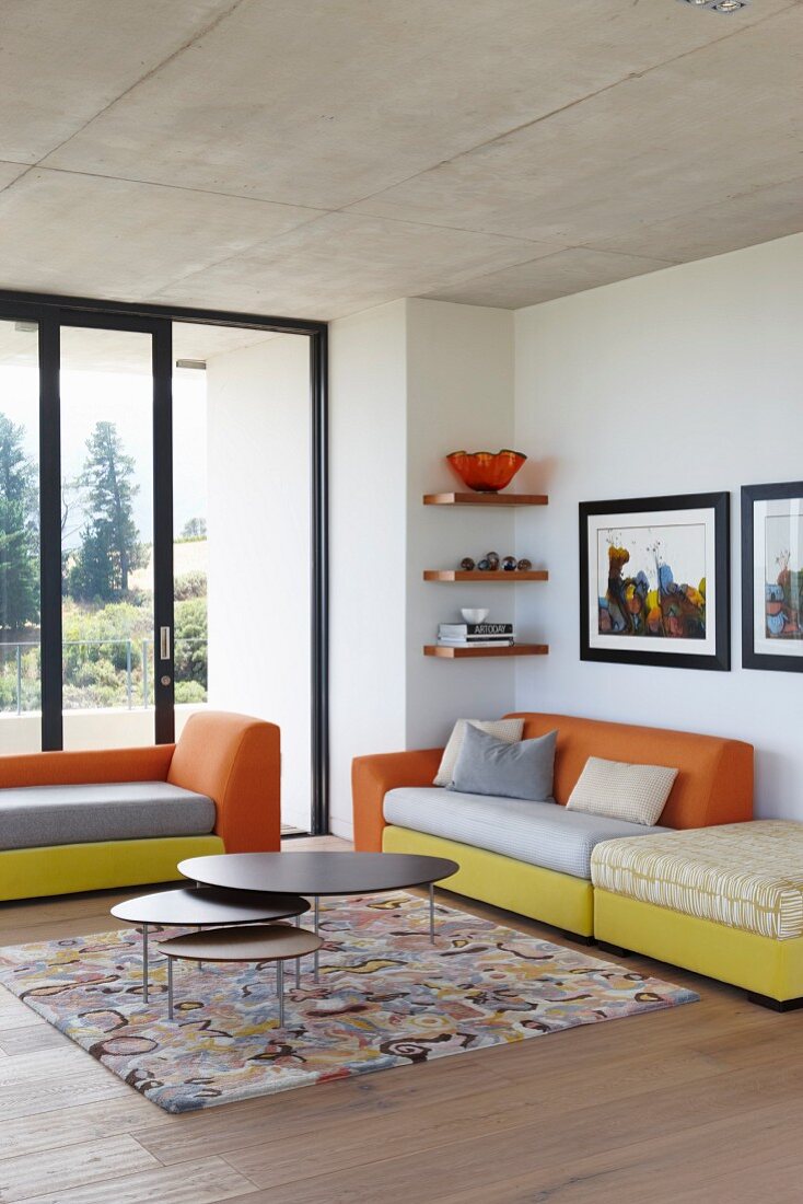 Modern sofas with colourful upholstered elements and nest of coffee tables in corner of minimalist interior with terrace doors