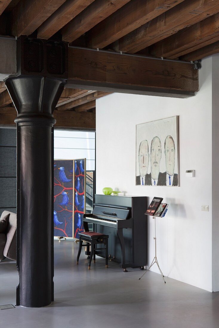 Black metal pillar under wooden beam structure with piano, bench and music stand in background