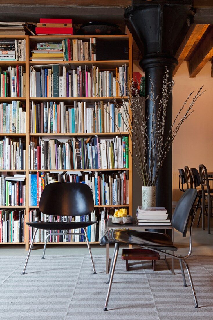 Schwarze Stühle im Retro Stil vor Bücherregal, seitlich schwarze Metallstütze in Loftwohnung