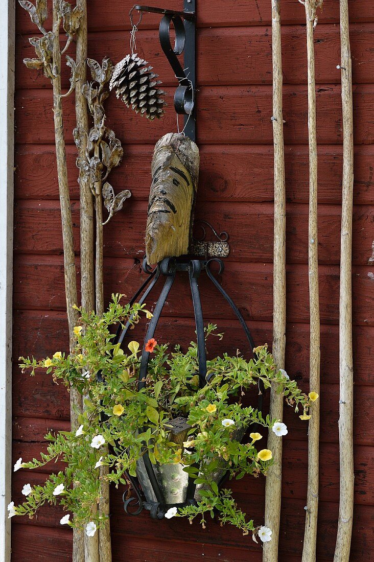 An Holzwand aufgehängter Blumentopf mit einjähriger Petunie und Holzkopf