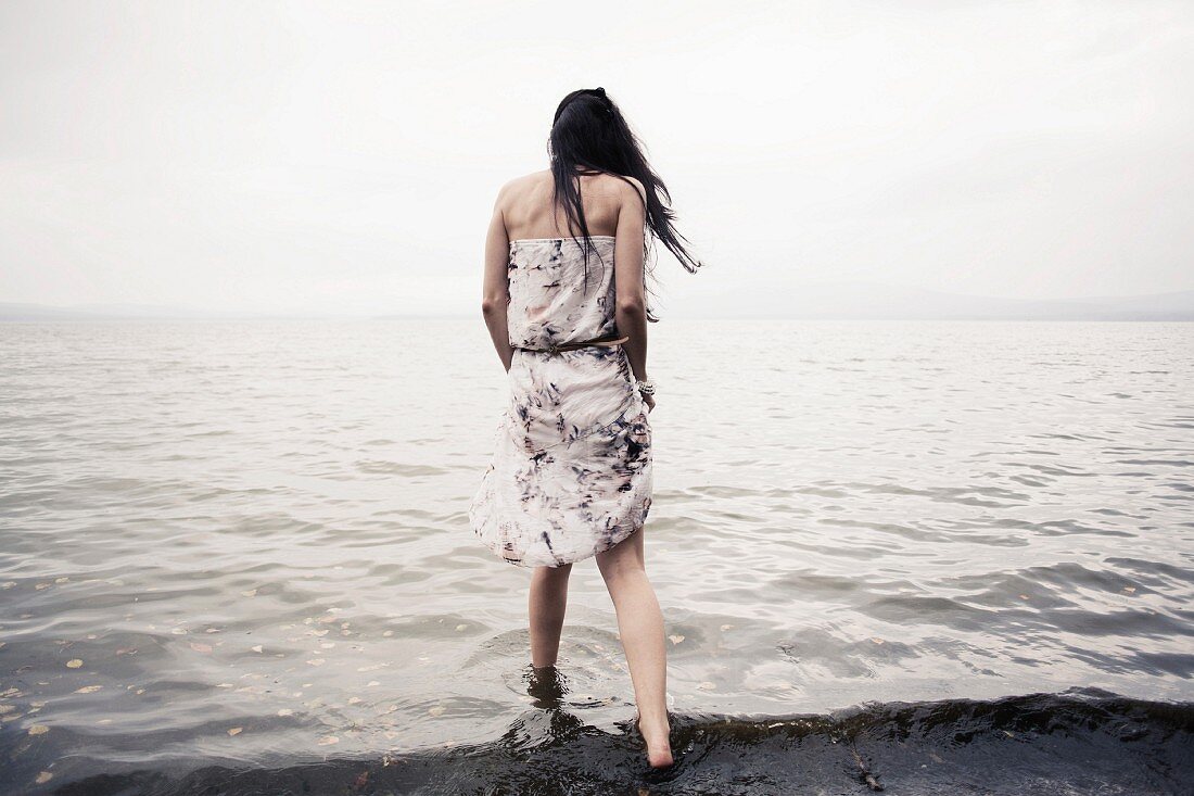 Frau im Sommerkleid läuft am Strand durchs Wasser