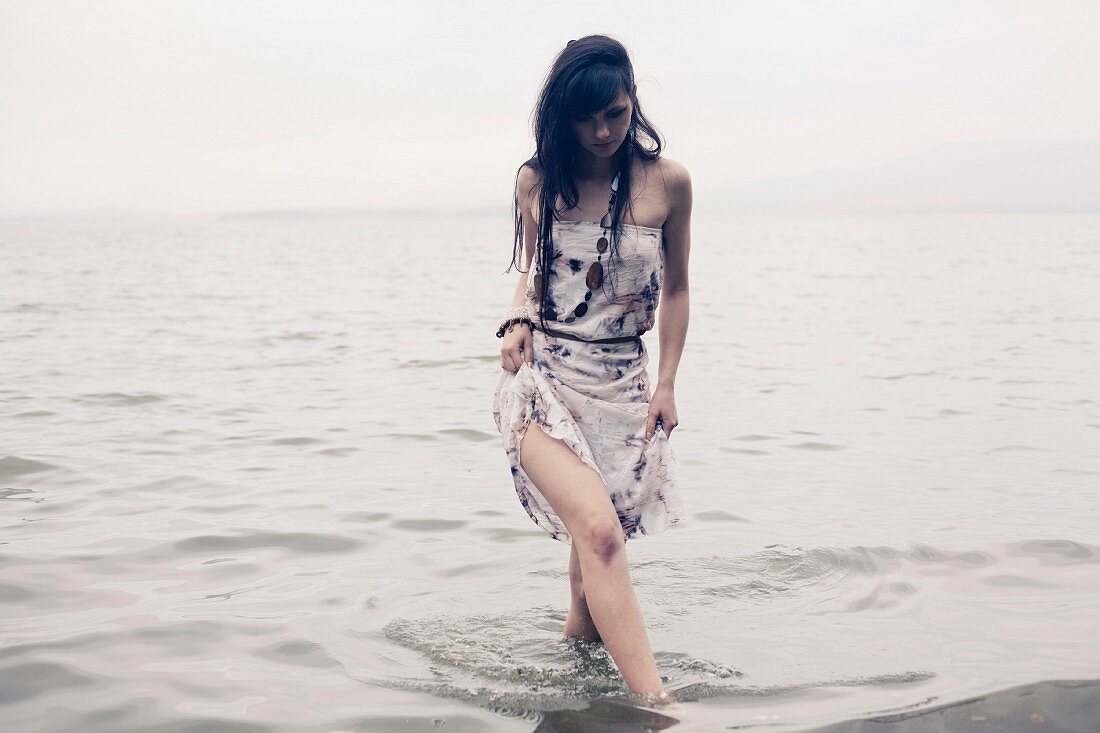 Woman wearing summer dress walking along beach through water