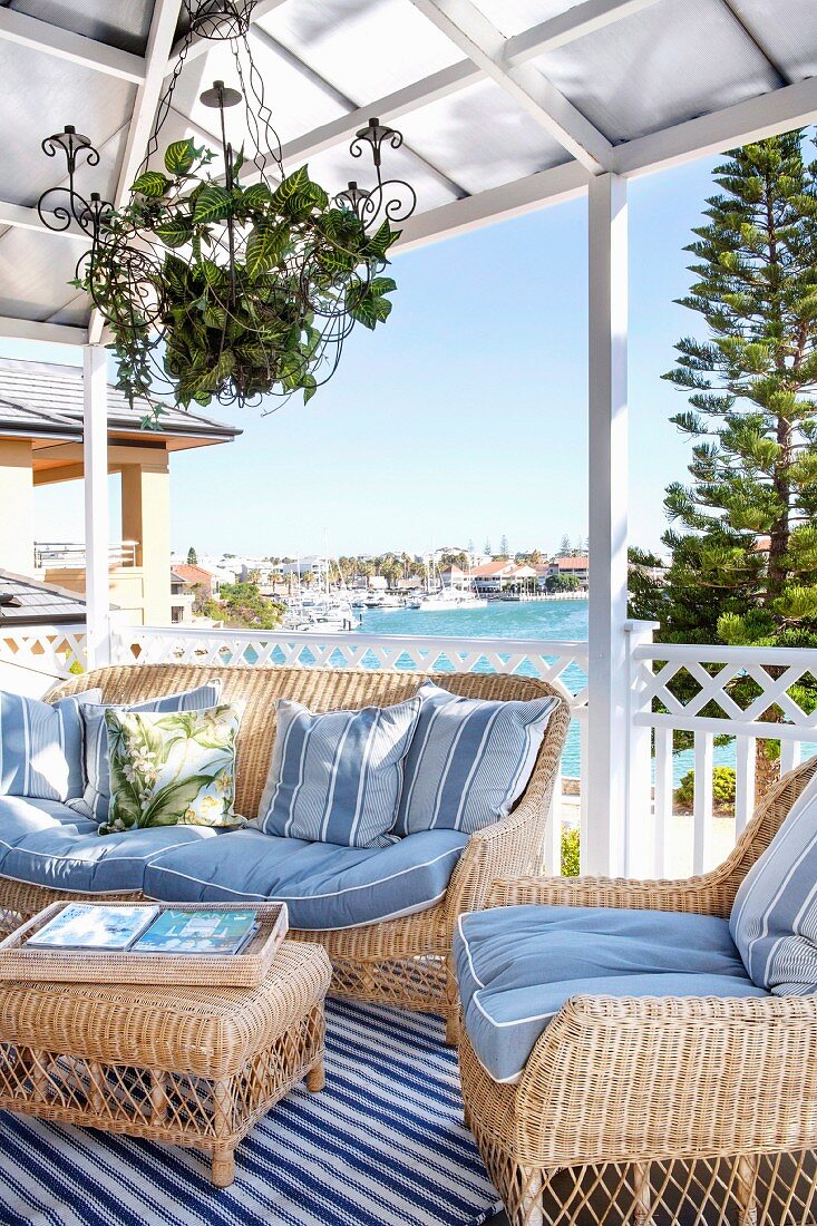 Pale wicker sofa set with pale blue cushions on roofed terrace with view of sea shore in background