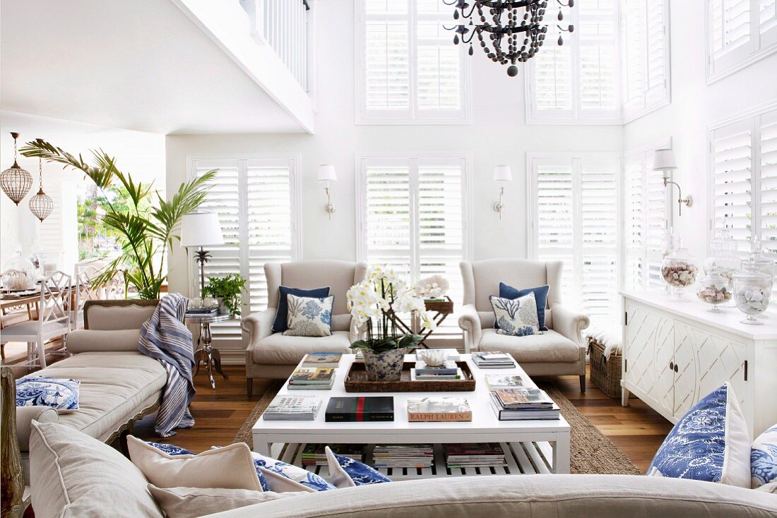 Naturfarbene Sitzmöbel um weißem Bodentisch, in nach oben offenem Wohnraum mit geschlossenen Fensterläden