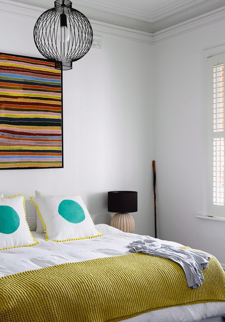Splashes of colour in white bedroom, wall-hanging above double bed and scatter cushions