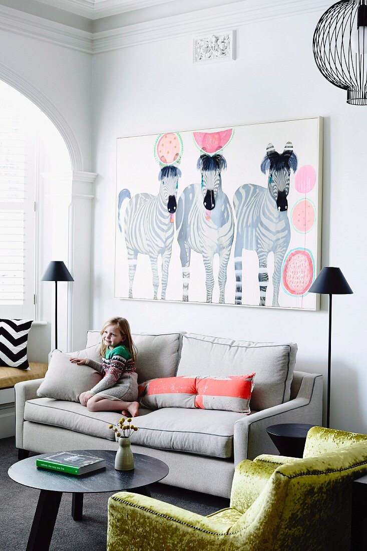 Kleines Mädchen auf einem Sofa, darüber ein Bild mit Zebramotiv, vorne ein goldgelb schimmernder Samtsessel