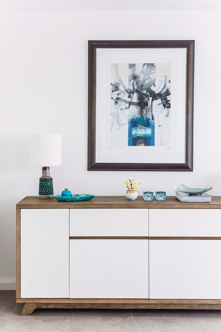 Sideboard mit Korpus aus Holz und weiss lackierten Fronten, vor Wand unter gerahmtem Bild