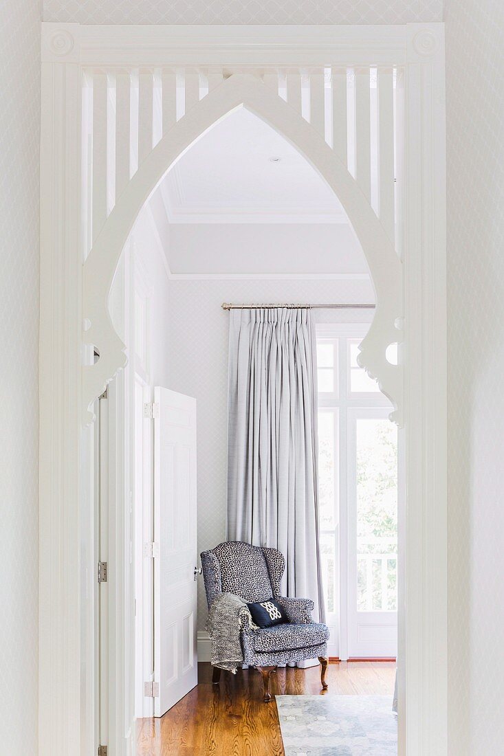 White-painted ogee arch built into doorway and view of comfortable armchair in front of French windows