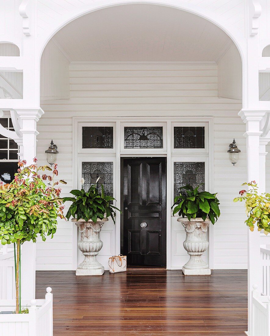 Veranda with white-painted archway and wooden floor leading to elegant front door flanked by antique planters