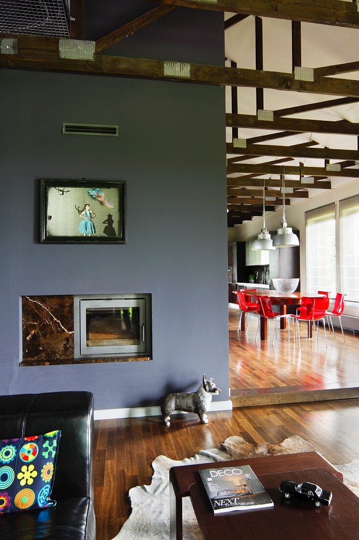 Lounge area in front of grey wall with integrated fireplace and view of dining area with red chairs in open-plan interior
