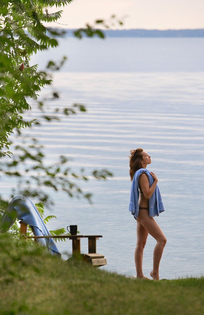 Woman wearing bikini and holding towel on shore of calm lake
