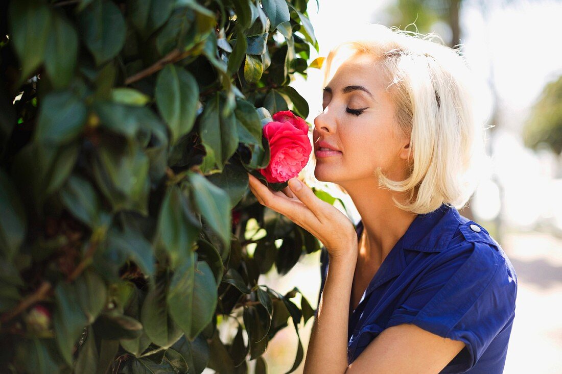 Blonde Frau riecht an einer duftenden Rose