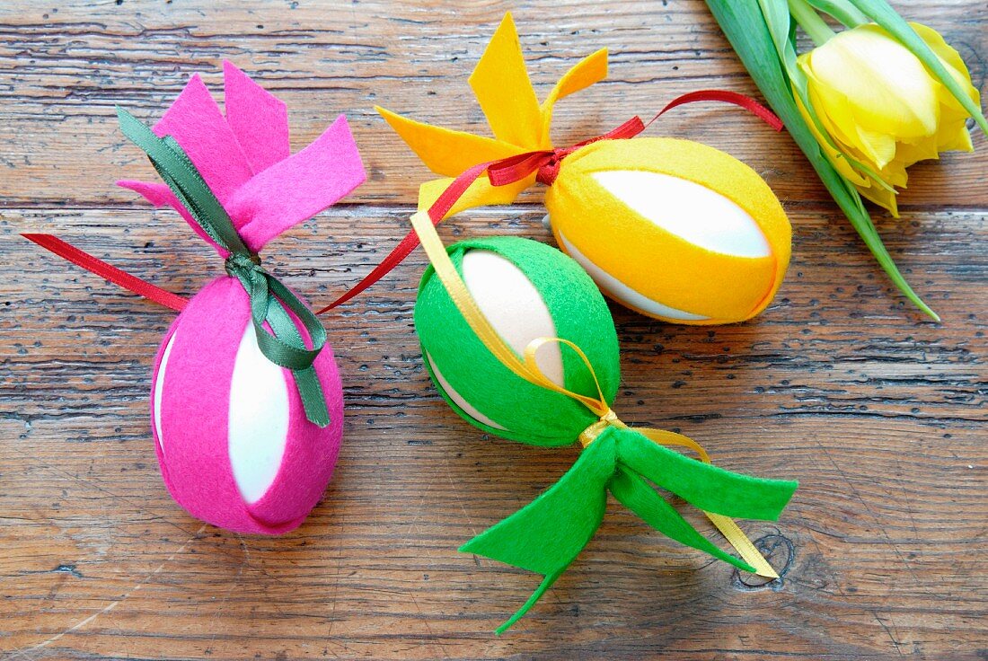 Easter decorations - eggs decorated with strips of colourful felt on wooden surface