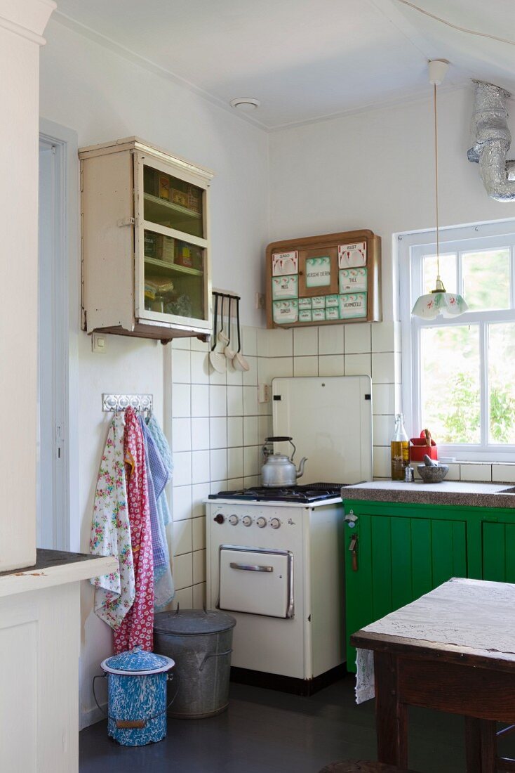 Vintage Gasherd vor gefliester Wand neben grün lackiertem Unterschrank vor Fenster, in schlichter Küche